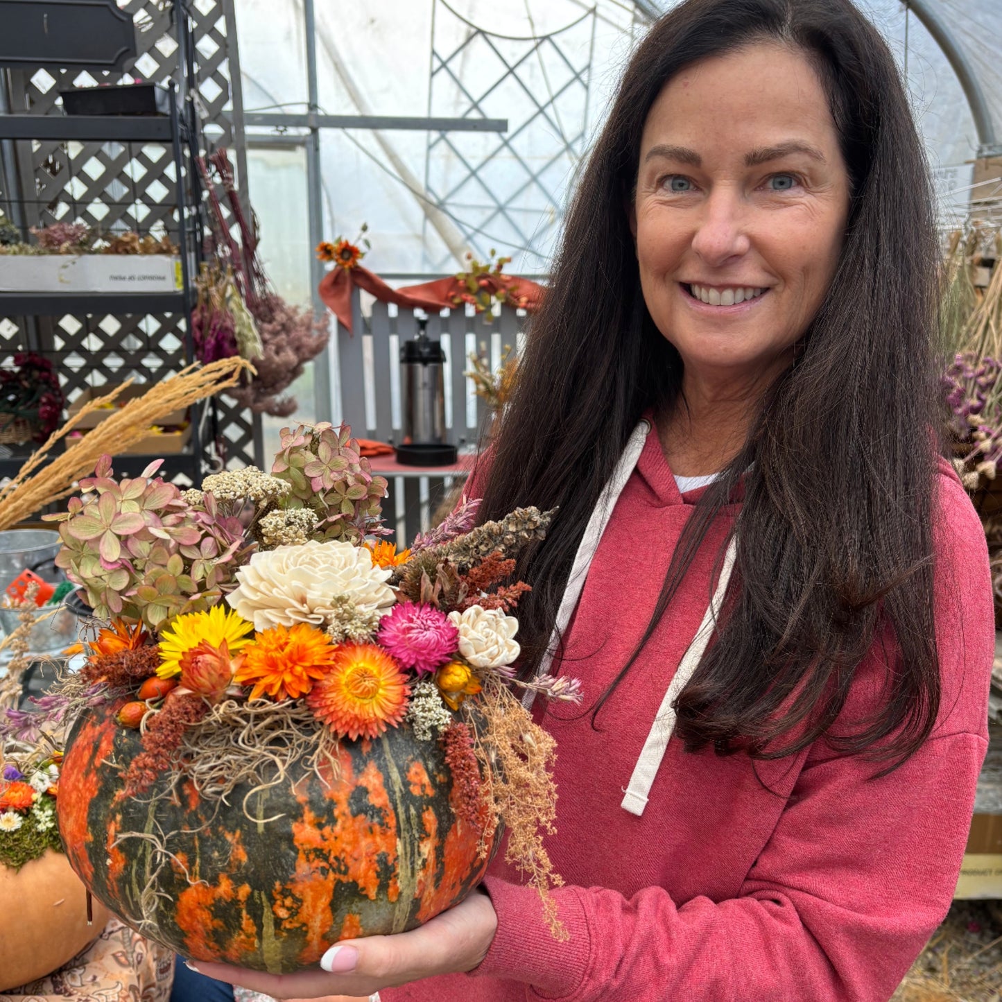 Woman holding a decorative pumpkin with flowers in a greenhouse setting
